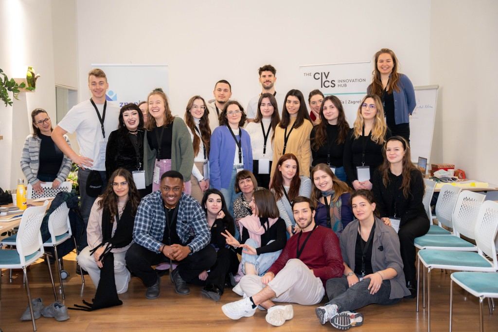 Around twenty workshop participants wearing lanyards posed in front of Civics Innovation Hub banners in Zagreb