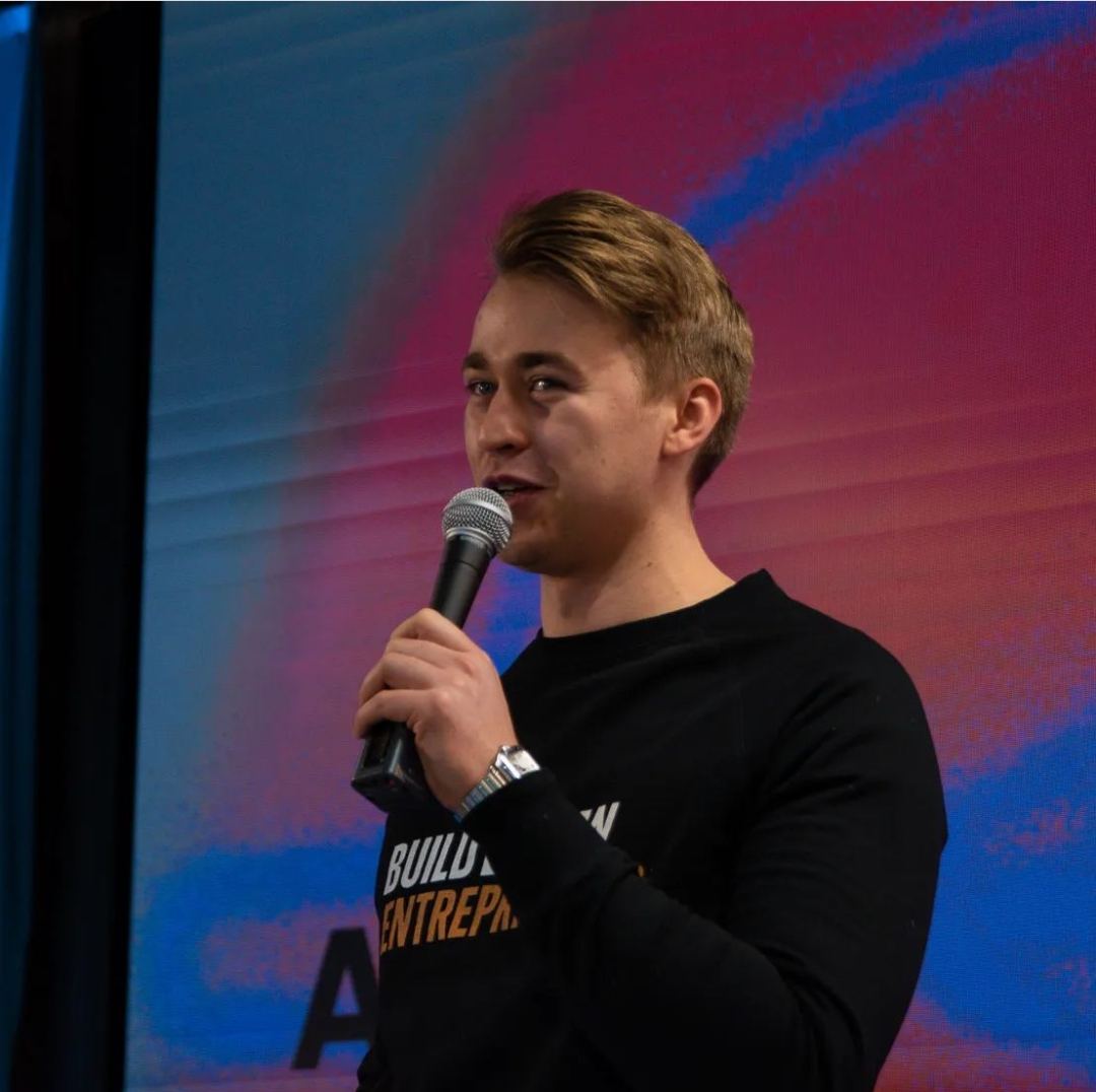 Host speaking with a handheld microphone in front of an LED screen at the Solve the SDGs hackathon in Helsinki
