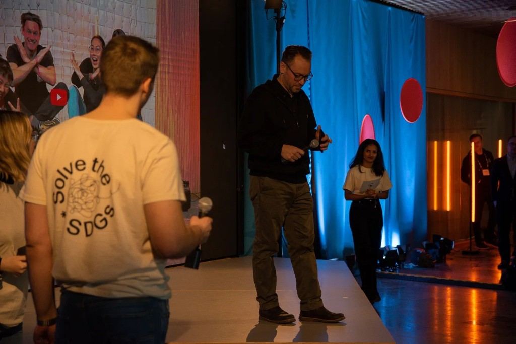 Two people with microphones on a low stage at the Solve the SDGs hackathon in Helsinki